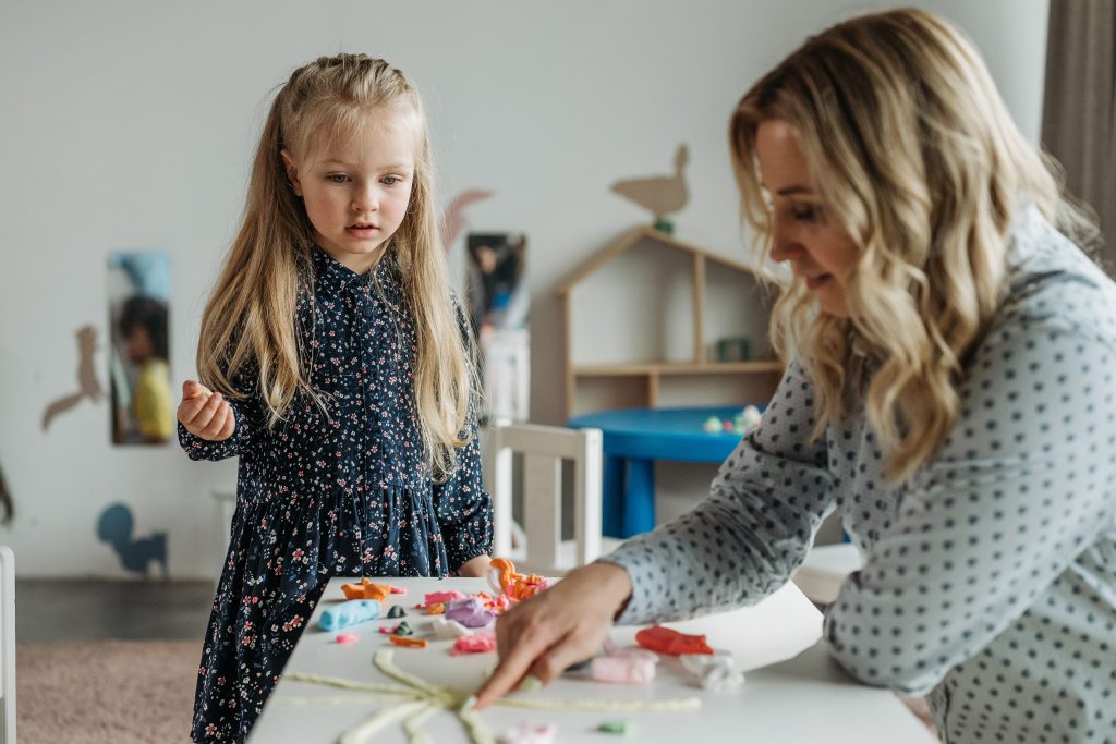 A young girl and a woman engage in a creative activity at a preschool classroom, fostering learning.